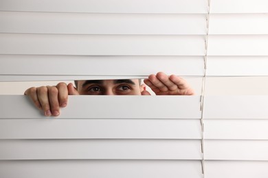 Photo of Young man looking through window blinds on white background