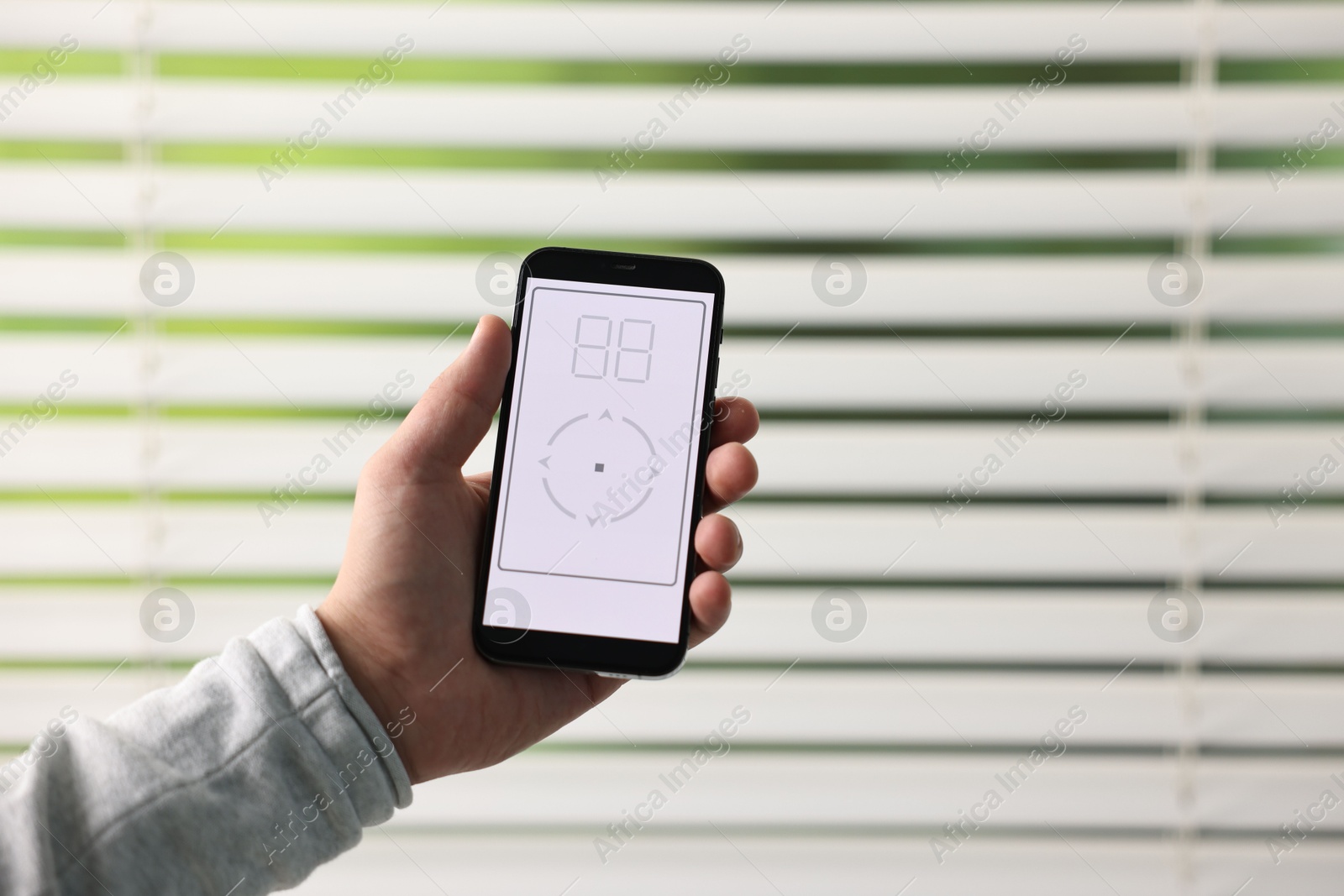 Photo of Man using phone to adjust window blinds indoors, closeup. Space for text