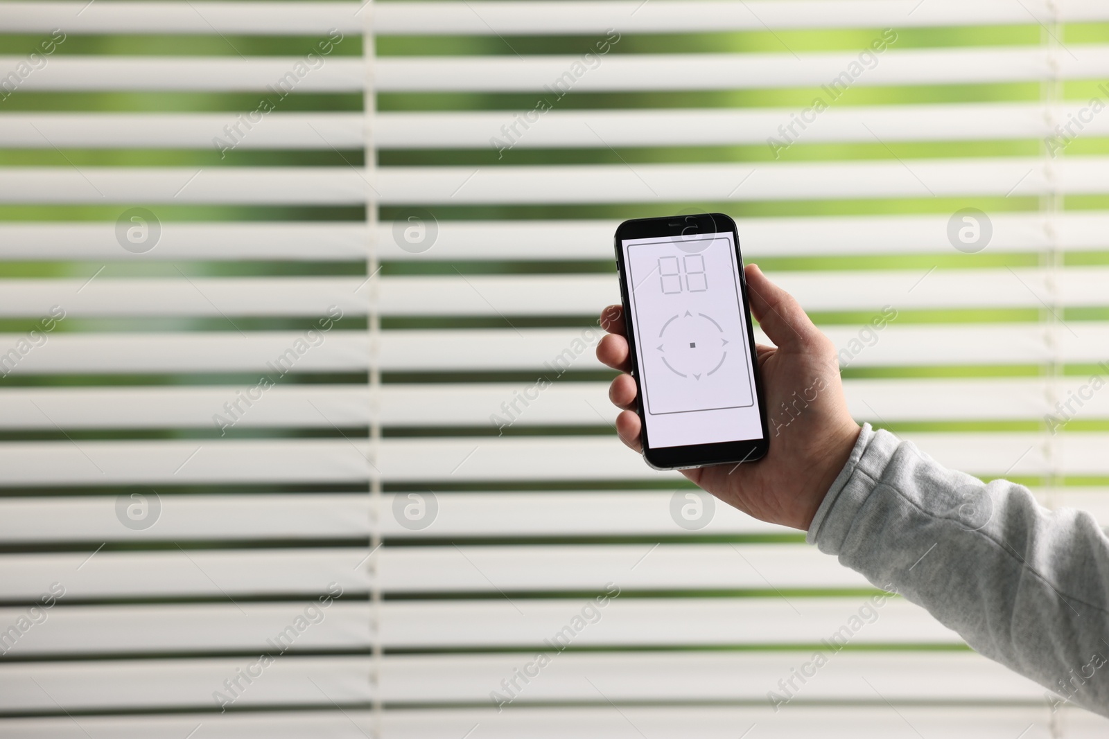 Photo of Man using phone to adjust window blinds indoors, closeup. Space for text