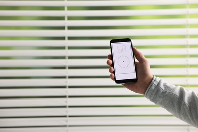 Man using phone to adjust window blinds indoors, closeup. Space for text