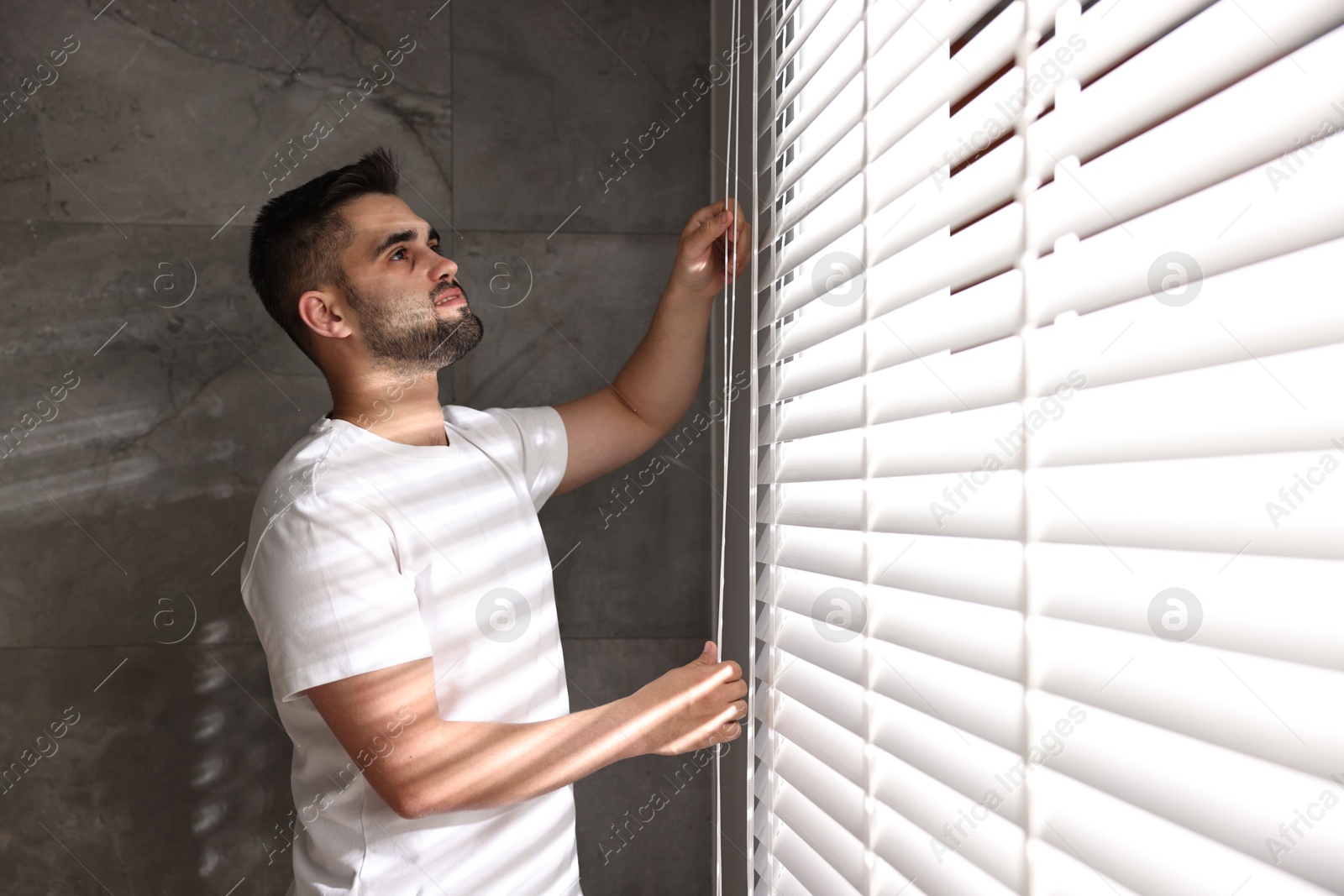 Photo of Man adjusting window blinds at home, space for text