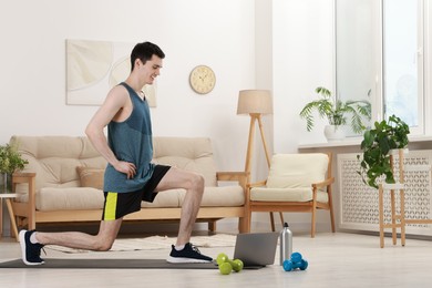 Online fitness trainer. Man doing exercise near laptop at home