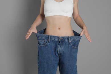 Photo of Woman in big jeans showing her slim body on grey background, closeup