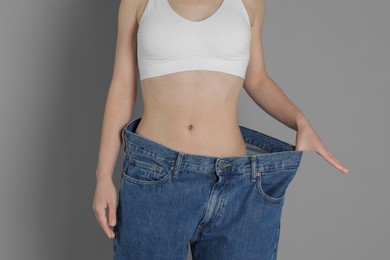 Photo of Woman in big jeans showing her slim body on grey background, closeup