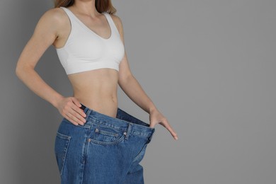 Photo of Woman in big jeans showing her slim body on grey background, closeup. Space for text