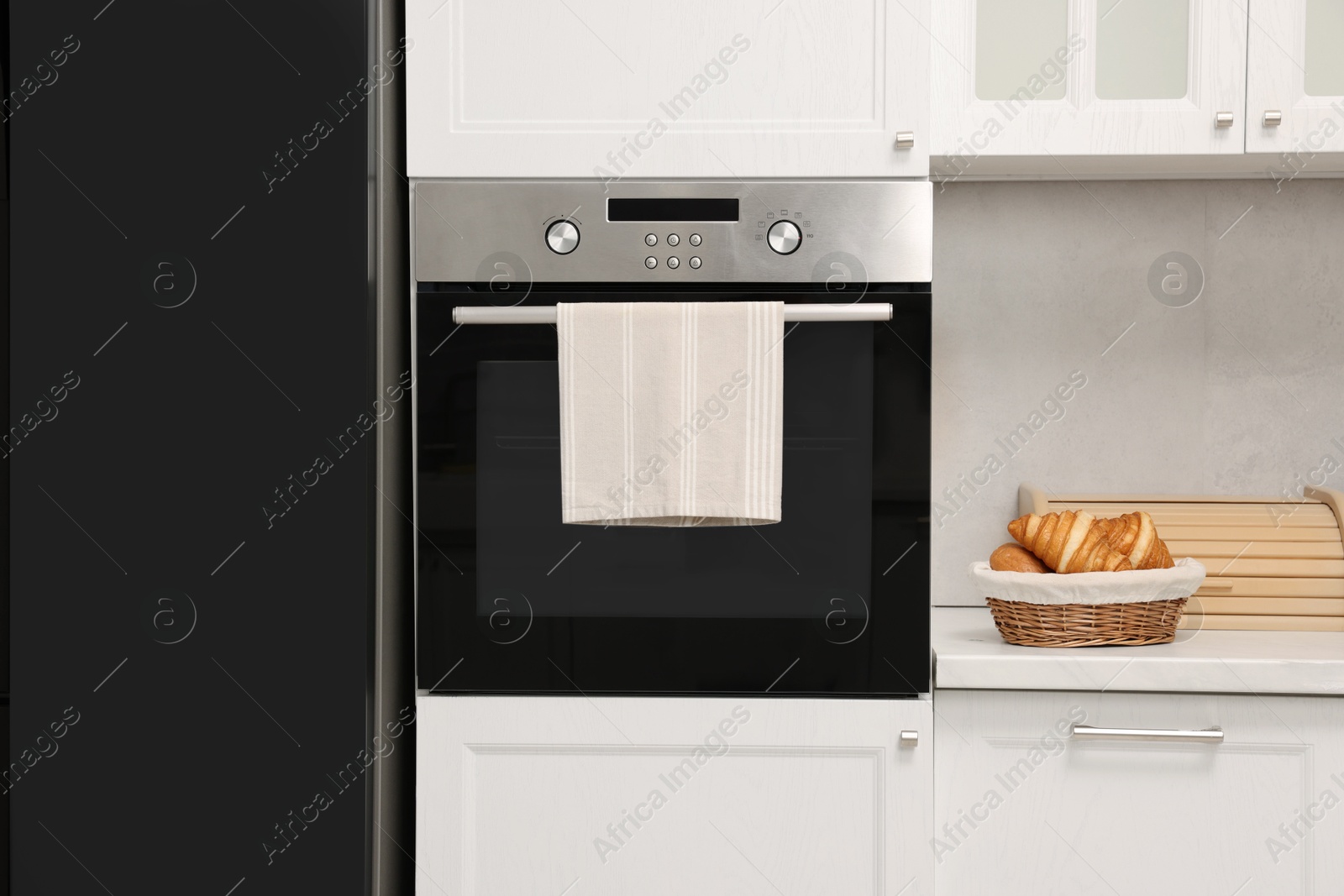 Photo of Electric oven with towel and croissants in kitchen. Cooking appliance