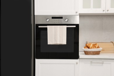 Electric oven with towel and croissants in kitchen. Cooking appliance