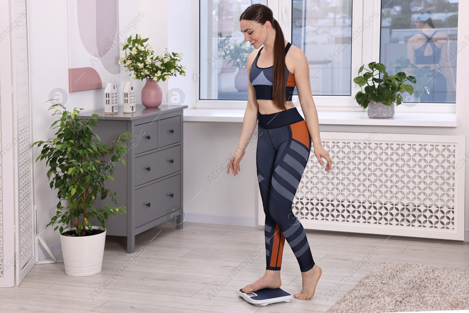 Photo of Happy woman stepping on floor scale at home