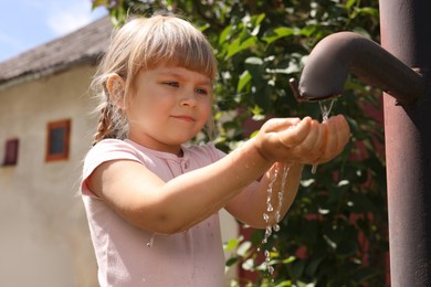 Photo of Water scarcity. Cute little girl drawing water with hands from tap outdoors