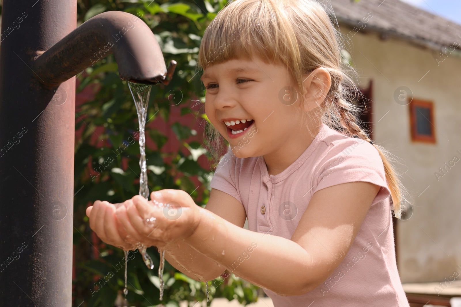 Photo of Water scarcity. Cute little girl drawing water with hands from tap outdoors