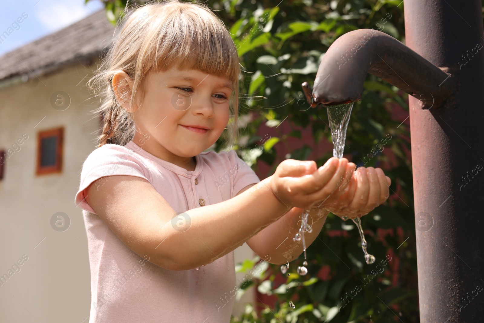 Photo of Water scarcity. Cute little girl drawing water with hands from tap outdoors