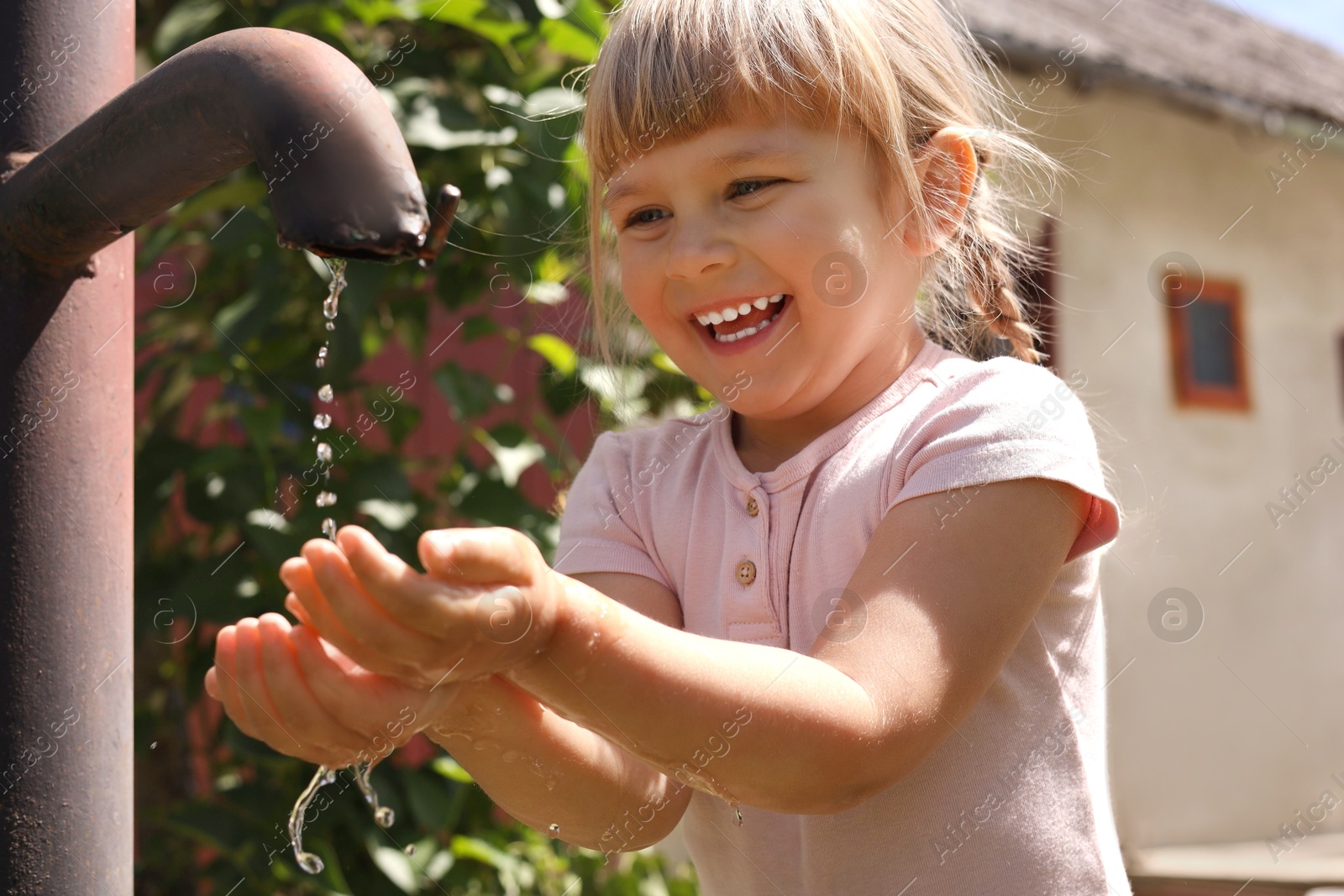 Photo of Water scarcity. Cute little girl drawing water with hands from tap outdoors