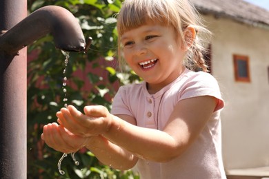 Photo of Water scarcity. Cute little girl drawing water with hands from tap outdoors