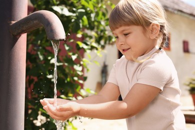 Photo of Water scarcity. Cute little girl drawing water with hands from tap outdoors