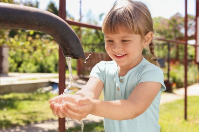 Photo of Water scarcity. Cute little girl drawing water with hands from tap outdoors