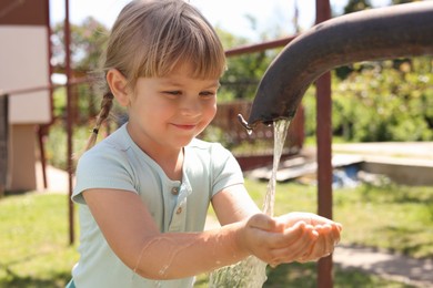 Water scarcity. Cute little girl drawing water with hands from tap outdoors