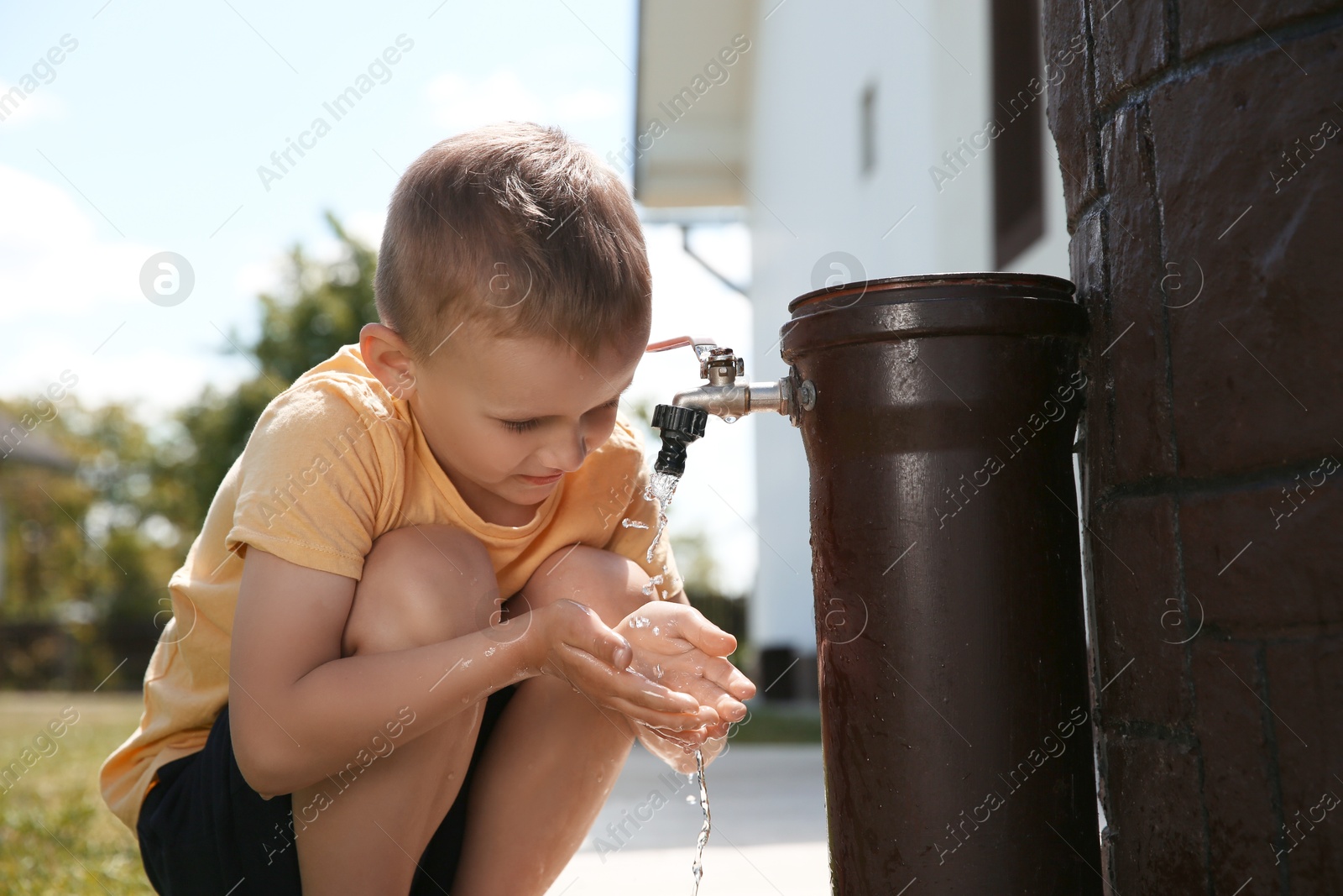 Photo of Water scarcity. Cute little boy drawing water with hands from tap outdoors