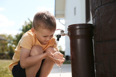 Photo of Water scarcity. Cute little boy drawing water with hands from tap outdoors