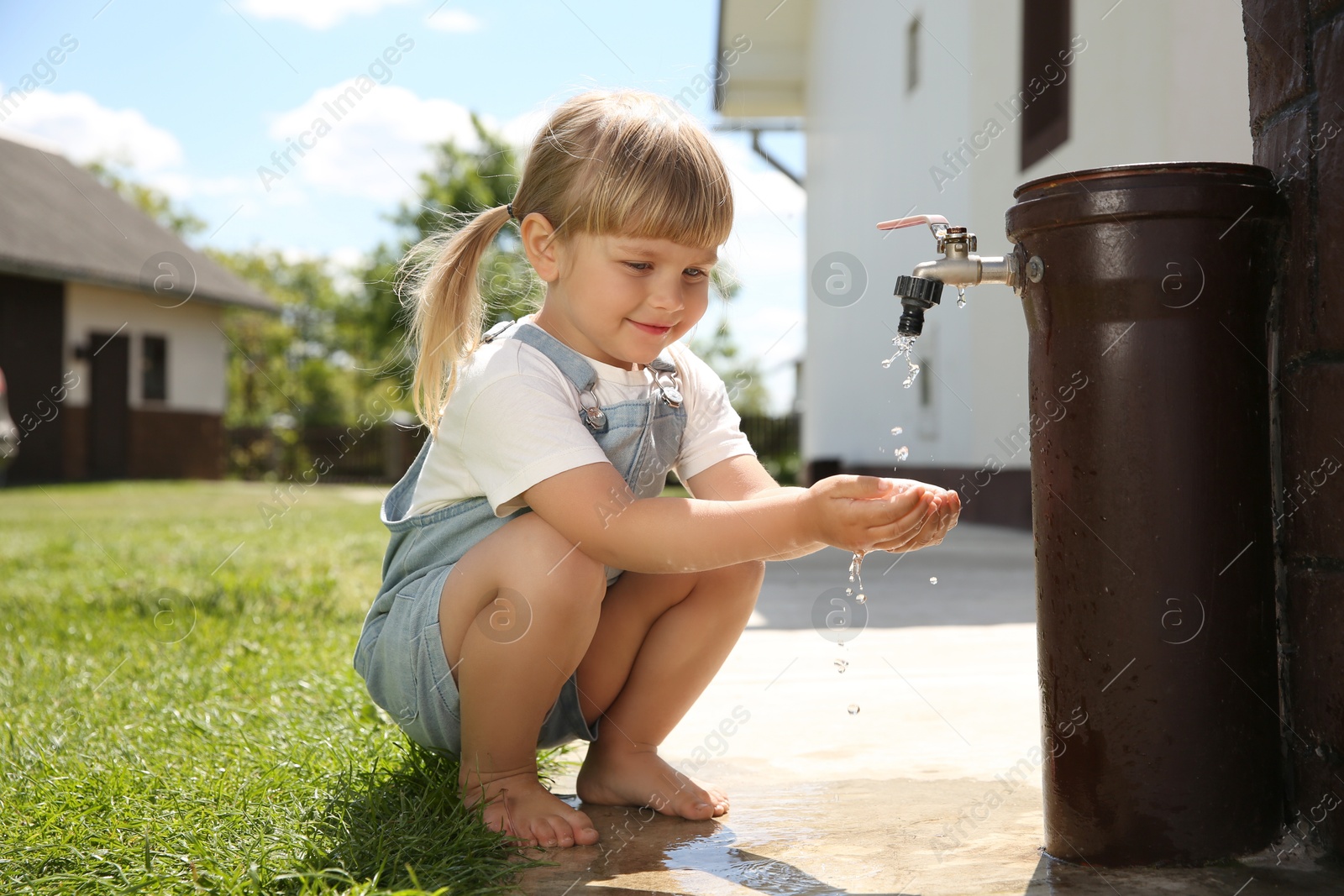 Photo of Water scarcity. Cute little girl drawing water with hands from tap outdoors