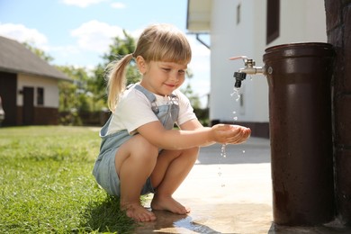 Water scarcity. Cute little girl drawing water with hands from tap outdoors