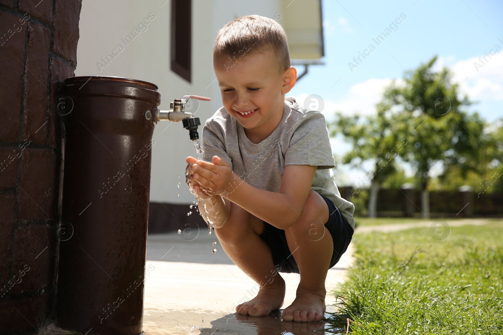 Photo of Water scarcity. Cute little boy drinking water from tap outdoors, space for text