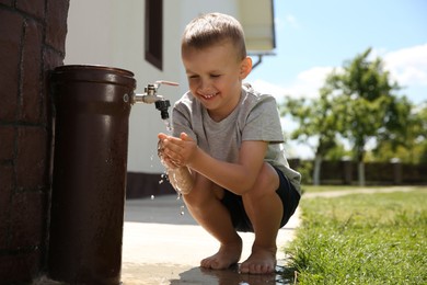 Photo of Water scarcity. Cute little boy drinking water from tap outdoors, space for text