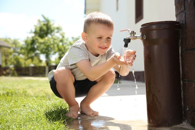 Photo of Water scarcity. Cute little boy drinking water from tap outdoors, space for text