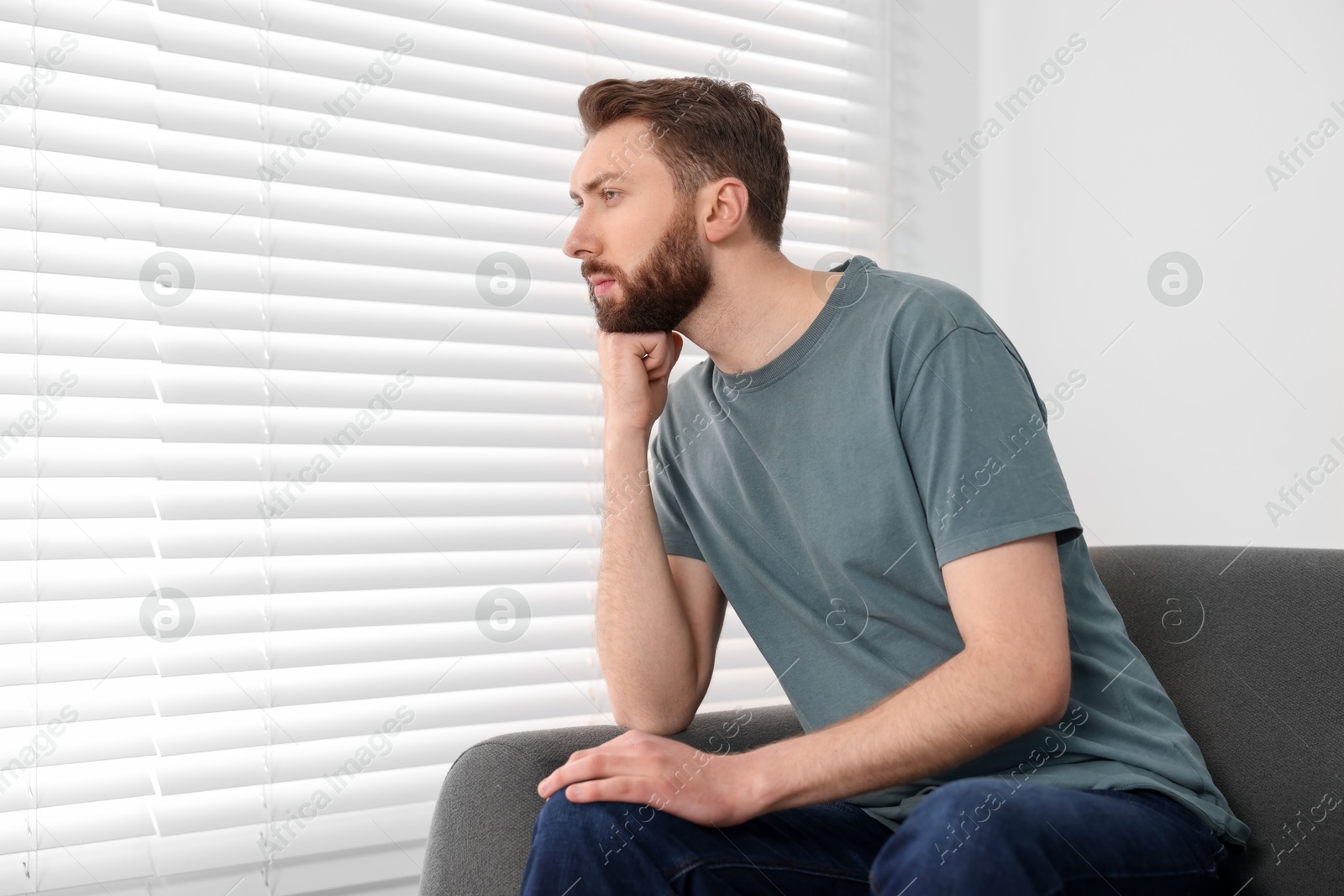 Photo of Loneliness concept. Sad man sitting on sofa at home, space for text