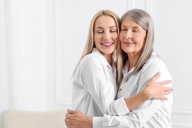 Family portrait of young woman and her mother near white wall. Space for text