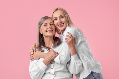 Family portrait of young woman and her mother on pink background