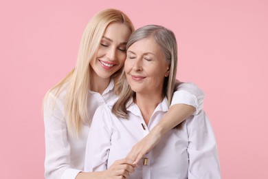 Family portrait of young woman and her mother on pink background