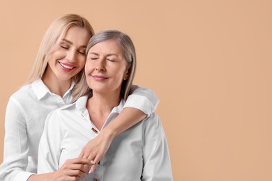 Family portrait of young woman and her mother on beige background. Space for text