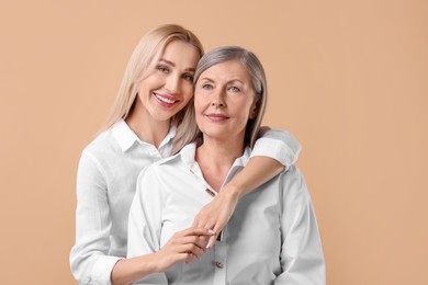 Family portrait of young woman and her mother on beige background