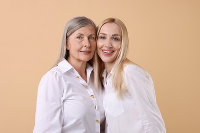 Family portrait of young woman and her mother on beige background