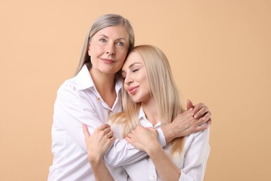 Family portrait of young woman and her mother on beige background