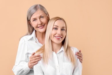 Family portrait of young woman and her mother on beige background. Space for text