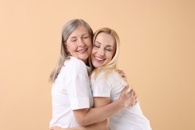 Family portrait of young woman and her mother on beige background