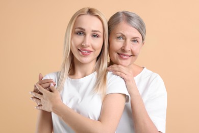 Family portrait of young woman and her mother on beige background