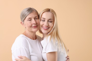 Family portrait of young woman and her mother on beige background