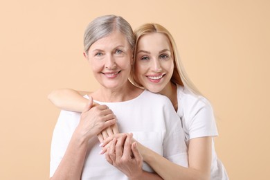 Family portrait of young woman and her mother on beige background