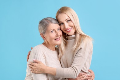 Family portrait of young woman and her mother on light blue background