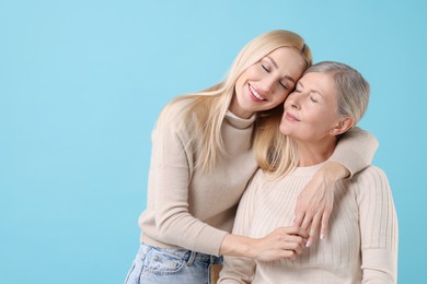 Photo of Family portrait of young woman and her mother on light blue background. Space for text