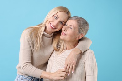 Family portrait of young woman and her mother on light blue background