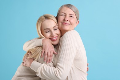 Family portrait of young woman and her mother on light blue background