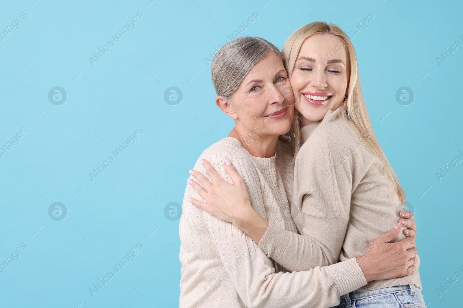 Photo of Family portrait of young woman and her mother on light blue background. Space for text