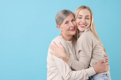 Family portrait of young woman and her mother on light blue background. Space for text