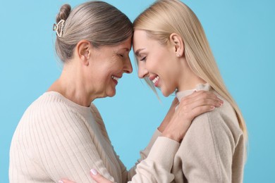 Family portrait of young woman and her mother on light blue background