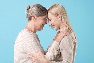 Family portrait of young woman and her mother on light blue background