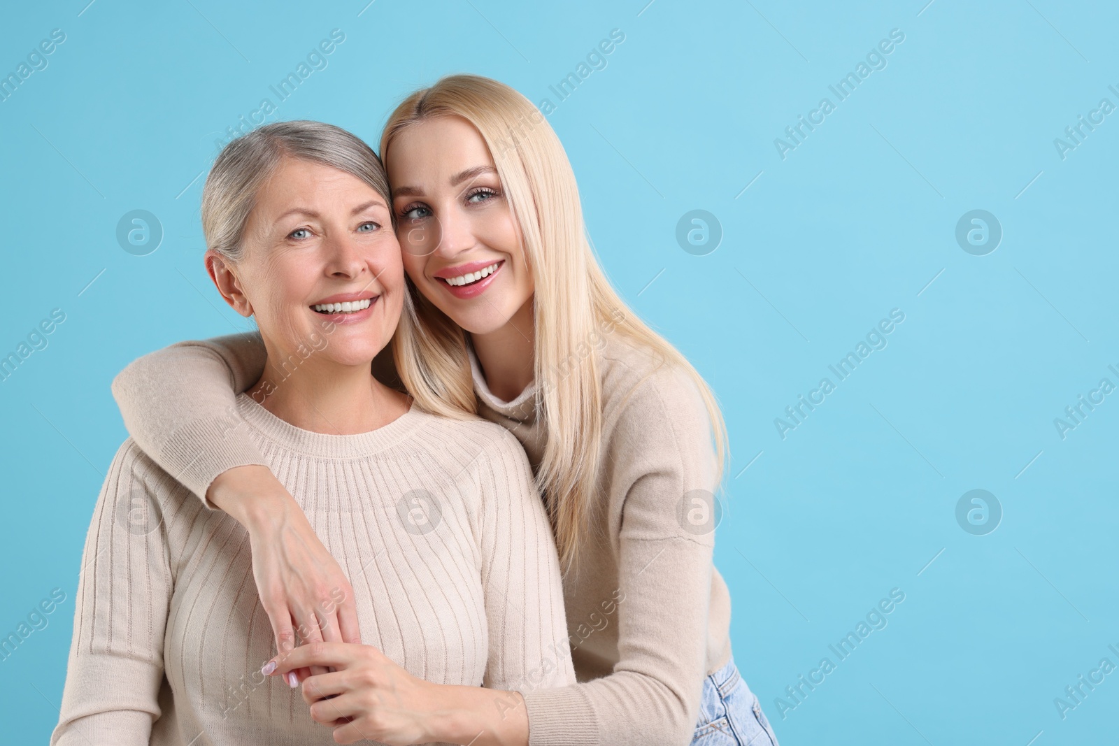 Photo of Family portrait of young woman and her mother on light blue background. Space for text