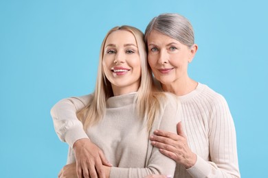 Family portrait of young woman and her mother on light blue background